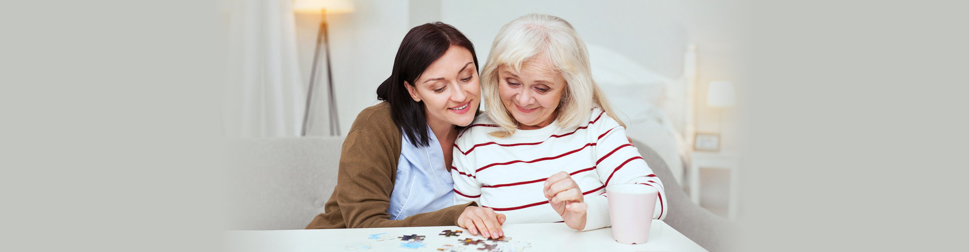 A woman and an older lady are playing with puzzle pieces.