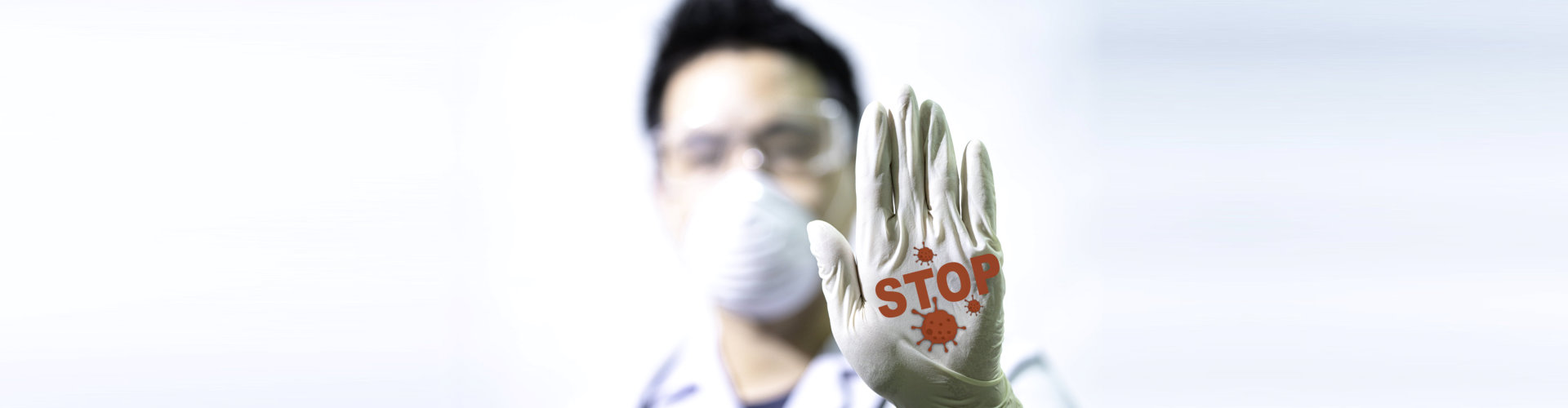 A doctor wearing gloves and a mask holding up his hand.